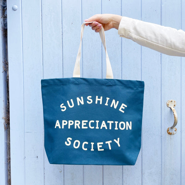 Large blue tote bag with sunshine appreciation sociaty slogan and white handle
