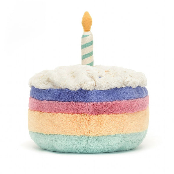 Soft fleece faux fur birthday cake doll with smiley face and little legs in corduroy. Ranbow layered cake with one candle. Cuddly plush toy.