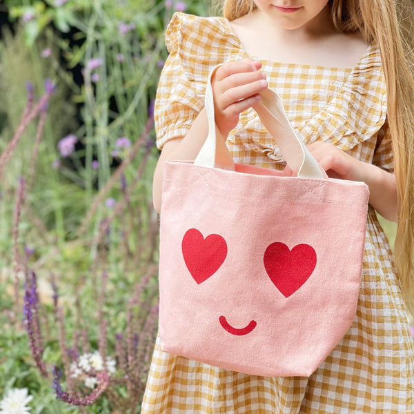 Small pink canvas tote bag with heart eyed smile face print and white handle