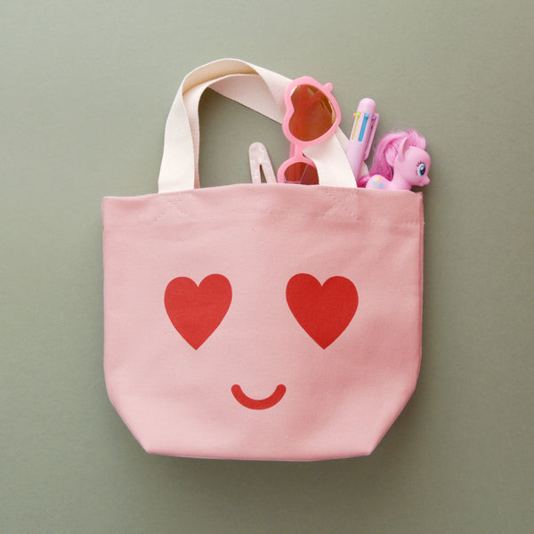 Small pink canvas tote bag with heart eyed smile face print and white handle